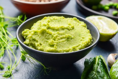 Koyu arkaplanda yeşil bezelye humusu olan bir kase, yakın plan.