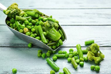 Renkli ahşap arka planda donmuş yeşil sebzeli kepçe