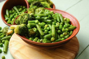 Renkli ahşap arka planda donmuş yeşil sebzeli kase, yakın plan.