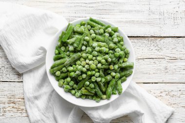 Açık ahşap arka planda donmuş yeşil sebzelerle dolu bir kase.