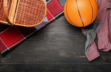 Koyu ahşap arka planda ekose, top ve kıyafetlerle piknik sepeti.