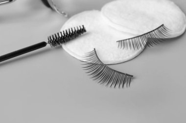 Takma kirpikler, pamuk pedler ve gri arka planda fırça, yakın plan.