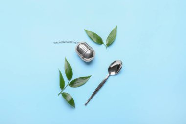 Tea strainer with green leaves and spoon on color background