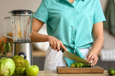 Mutfakta salatalık kesen genç bir kadın.