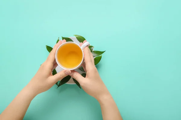 Женские Руки Чашкой Чая Зелеными Листьями Цветном Фоне — стоковое фото