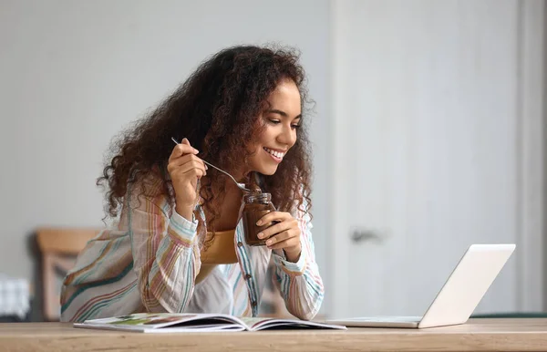 Jovem Afro Americana Comendo Pasta Chocolate Enquanto Usa Laptop Cozinha — Fotografia de Stock