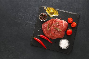 Board with raw beef meat and vegetables on dark background