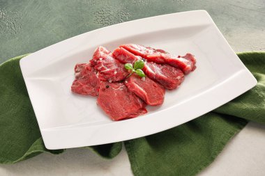 Plate with raw beef meat slices on light background