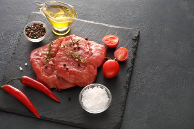 Board with raw beef meat and vegetables on dark background