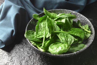 Koyu arkaplanda taze ıspanak yapraklı tabak.