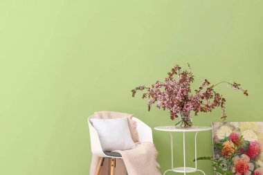 Masanın üzerinde çiçek açan dalları ve renkli duvarın yanında koltuğu olan vazo.