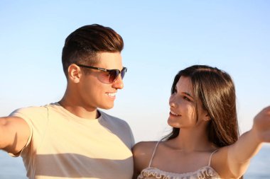 Mutlu genç çift deniz sahilinde selfie çekiyor.