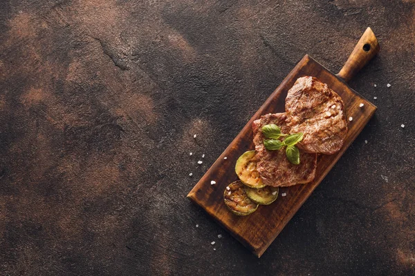 Houten Bord Met Lekkere Rundersteaks Gegrilde Groenten Grunge Achtergrond — Stockfoto