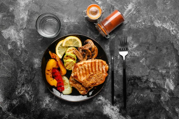 Plate with tasty grilled vegetables and steaks on grey background