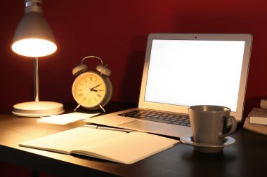 Modern dizüstü bilgisayarı ve renkli duvarın yanında parlayan lambası olan şık bir iş yeri.