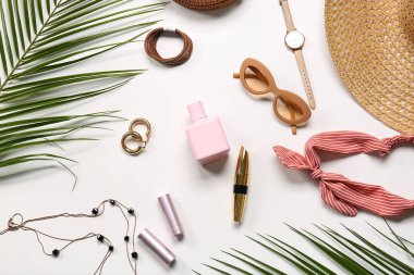 Beyaz arka planda kadın aksesuarları, kozmetik ürünleri ve palmiye yaprakları olan kompozisyon