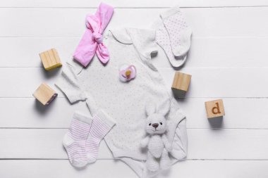Hafif ahşap arka planda bebek kıyafetleri, oyuncaklar ve aksesuarlarla kompozisyon