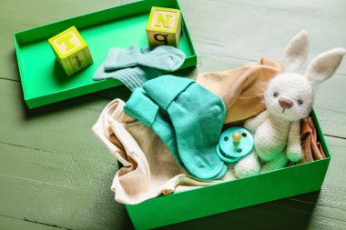 Bebek kıyafetleriyle dolu bir kutu, emzik ve oyuncak renkli ahşap arka plan, yakın plan