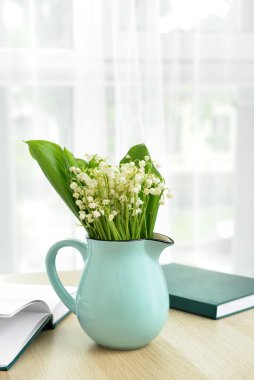 Pencerenin yanındaki masada vadi zambağı çiçekleri olan vazo.