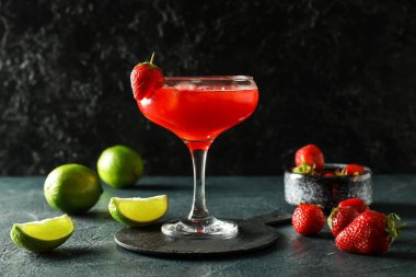 Glass of strawberry daiquiri cocktail, limes and berries on dark background