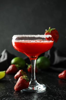 Glass of strawberry daiquiri cocktail, limes and berries on dark background