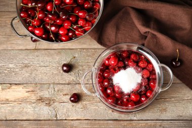 Glass pot with sweet cherry and sugar on wooden background