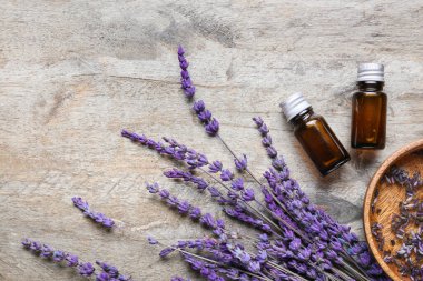 Bottles of lavender essential oil and flowers on wooden background