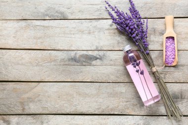 Bottle of lavender essential oil, scoop with sea salt and flowers on wooden background