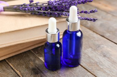 Bottles of lavender essential oil, books and flowers on wooden background