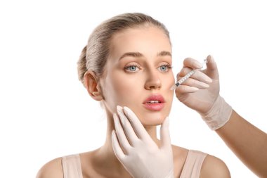 Genç bir kadın, dudaklarından beyaz arka plana enjeksiyon yaptırıyor.