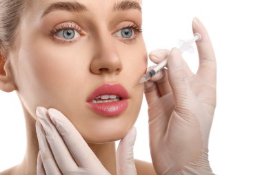 Genç bir kadın, dudaklarından beyaz arka plana enjeksiyon yaptırıyor.