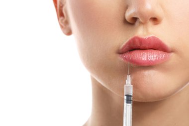 Genç bir kadın dudaklarından beyaz arka plana doğru enjeksiyon yaptırıyor.