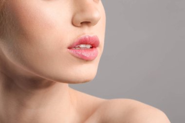 Gri arka planda güzel dudakları olan genç bir kadın, yakın plan.