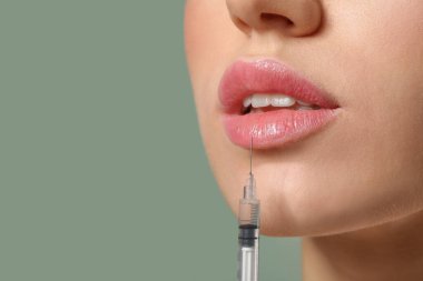 Dudaklarından renk arkaplanına karşı doldurucu enjeksiyon alan genç kadın, yakın plan