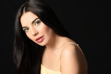 Koyu arkaplanda şık makyajlı güzel bir genç kadın.