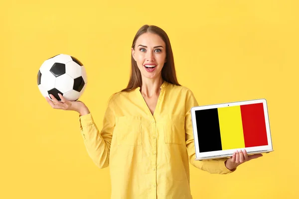年轻女子拿着足球和笔记本电脑 屏幕上有比利时国旗 背景是彩色的 — 图库照片