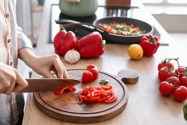 Woman cutting bell pepper in kitchen, closeup