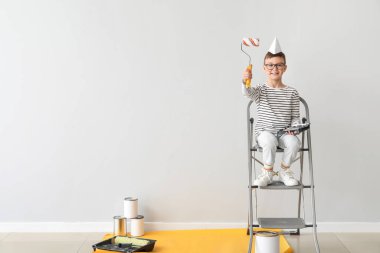 Işık duvarının yanında boya silindirli şirin bir çocuk.