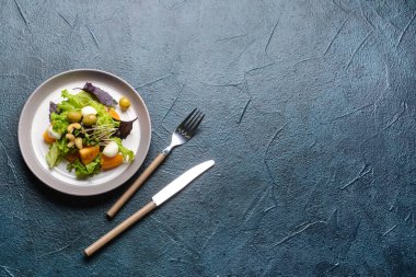 Koyu arkaplanda lezzetli taze salata ve çatal bıçak takımı tabağı.