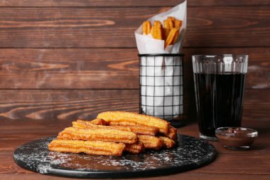 Lezzetli churros tabağı, bir bardak kola ve ahşap zemin üzerinde erimiş çikolata sosu.