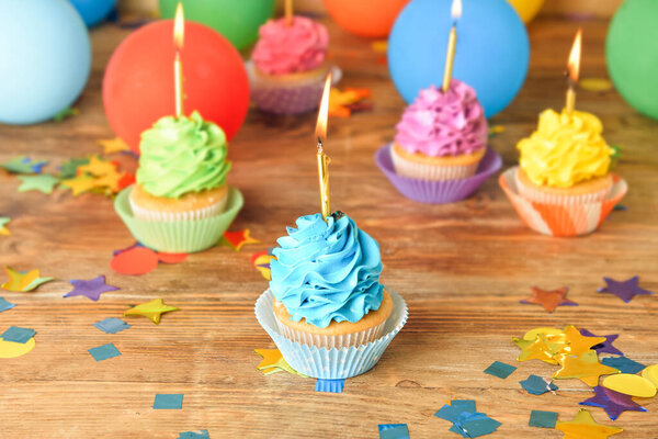 Tasty Birthday cupcakes with burning candles on wooden background