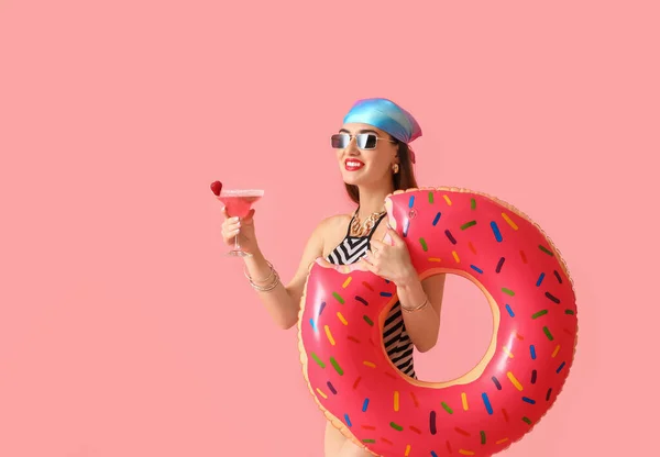 Beautiful young woman with cocktail and swimming ring on color background