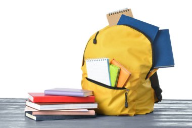 Okul çantası ve defterler beyaz arka plana karşı ahşap masaya.