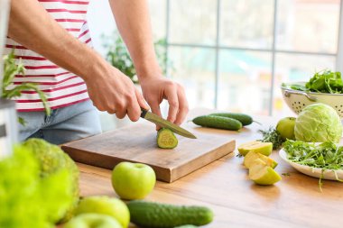 Genç adam mutfakta salatalık kesiyor.