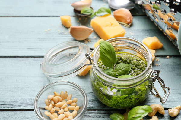 Jar with fresh pesto sauce and ingredients on color wooden background