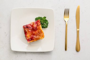 Hafif arka planda lezzetli sebzeli lazanya ve çatal bıçak takımı.