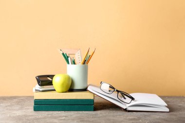 Renkli duvarın yanındaki masada kırtasiye, gözlük ve elma bulunan kitaplar.
