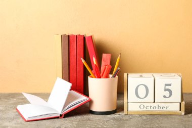 Renk duvarının yanındaki masada kırtasiye malzemesi ve kitaplarla dolu küp takvimi