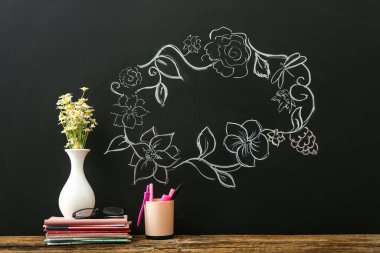 Sınıfta papatya çiçekli vazo ve kırtasiye malzemesi var.