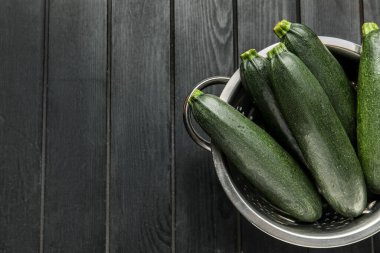 Koyu ahşap arka planda taze kabak kabakları olan Colander, yakın plan.